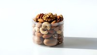 Mixed nuts assortment in glass jar with almonds, walnuts, cashews and pecans isolated on white background for healthy snacking and cooking.