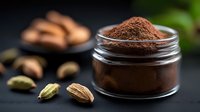Ground cardamom powder in glass jar with whole cardamom pods and spices scattered on dark background, aromatic Indian seasoning for cooking and baking.