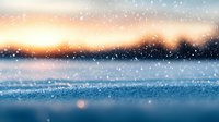 Magical winter landscape with falling snow at sunset, glittering frost crystals on blue surface create dreamy atmosphere against orange sky background.