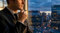 Thoughtful businessman in suit contemplating city skyline at dusk from office window, urban professional planning strategy during evening hours.