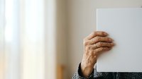Senior adult with medium skin tone holding blank white board or sign, suitable for advertising, marketing campaigns, promotional messaging, and business communications.