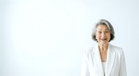 Senior woman with gray hair wearing white blazer smiling at camera against neutral background, suitable for corporate, healthcare, business and professional portraits.