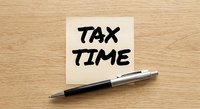 Sticky note with tax time reminder and pen on wooden desk surface for accounting and financial planning preparation during filing season.