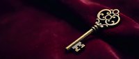 Ornate vintage brass key with decorative scrollwork handle resting on luxurious deep red velvet fabric surface creating elegant antique atmosphere.