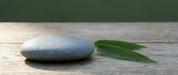 Smooth zen stone with green bamboo leaves on rustic wooden surface, evoking calm, balance, and mindfulness in spa and wellness concepts.