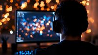 Silhouette of person gaming at night with bokeh lights and monitor screen glow creating atmospheric mood for entertainment and leisure activities.