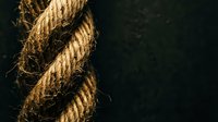 Twisted natural jute rope with frayed fibers against dark background, rustic nautical marine cordage texture for craft and industrial applications.