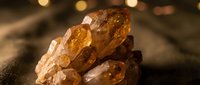 Amber crystals with warm golden tones stacked together on dark surface with soft bokeh lighting in background, suitable for mineral, geology, and wellness content.
