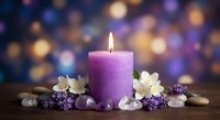 Purple candle burning with white flowers, lavender sprigs and smooth stones on wooden surface against colorful bokeh background for spa relaxation.