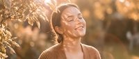 Young woman enjoying peaceful moment in golden sunlight outdoors with eyes closed and gentle smile, expressing joy and serenity in warm autumn light.