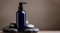 Dark blue glass pump bottle for cosmetics or essential oils on smooth spa stones against neutral brown background, minimalist wellness composition.