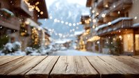 Rustic wooden table with blurred winter village scene in background, snow falling and festive lights creating cozy holiday atmosphere.