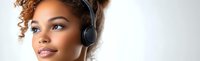 Young African American woman with natural curly hair wearing wireless headphones smiles confidently against light background, enjoying music in modern lifestyle setting.