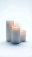 Three white pillar candles of different heights glowing softly on a light background, creating a warm, serene ambiance for home decor.