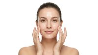 Young Caucasian woman applying skincare cream to face with gentle massage motions on white background for beauty and wellness advertising campaigns.