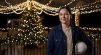 Young Hispanic woman smiling outdoors with festive string lights creating warm bokeh background for holiday celebrations and winter events.