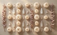 Autumn flat lay pattern with white pumpkins, dried eucalyptus branches and candles arranged in rows on neutral beige background for seasonal decor.
