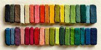 Colorful chalk pastels arranged in rainbow spectrum on textured paper surface for artistic drawing and creative projects.