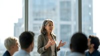 Professional businesswoman presenting to corporate team in modern office conference room with city skyline view for business meetings and presentations.