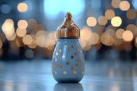 Blue baby bottle with golden polka dots pattern on blurred bokeh background. Soft focus creates dreamy atmosphere for nursery and childcare concepts.