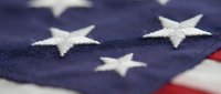 Close-up macro view of American flag fabric showing white embroidered stars on deep blue field with red and white stripes visible in soft focus background.