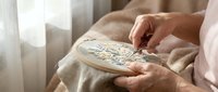 Woman hands embroidering colorful floral pattern on fabric with hoop in cozy home interior. Traditional needlework craft hobby for relaxation and creativity.