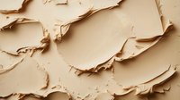 Creamy beige foundation texture with rough smeared surface showing cosmetic product consistency and makeup application texture background pattern.