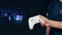 Gamer holding white wireless controller with blurred gaming setup in background, male player in dark shirt ready for online gaming session or esports competition.