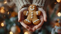 Hands in cozy sweater holding freshly baked gingerbread man cookie against blurred Christmas lights background, creating warm holiday atmosphere.