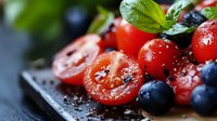 Fresh cherry tomatoes with blueberries and basil leaves on dark background, water drops on red tomatoes, macro food photography with selective focus.