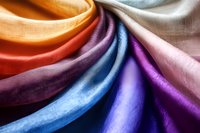 Colorful silk fabric swatches arranged in flowing waves showing vibrant rainbow hues from orange to purple, perfect for textile and fashion design projects.