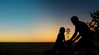 Adult male and young female child planting sapling together at sunset, silhouetted against golden sky. Environmental conservation and family bonding concept for eco-friendly initiatives.