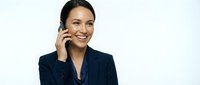 Young woman with dark hair and olive complexion, wearing a navy blazer, smiling while speaking on a mobile phone against a white background. Suitable for business, communication, and professional lifestyle content.