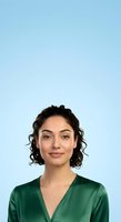 Young woman with shoulder-length curly dark hair and olive complexion wearing forest green v-neck shirt against light blue background. Professional headshot suitable for corporate profiles, business websites, and recruitment materials.