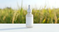 White dropper bottle with pipette on table against blurred green field background. Natural organic skincare serum cosmetic product for beauty treatment.