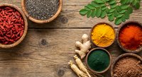 Colorful superfood ingredients in wooden bowls on rustic table including goji berries, chia seeds, turmeric, paprika and spirulina powder for healthy cooking.