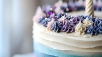 Elegant birthday cake decorated with purple and cream buttercream swirls, gold candle on pastel blue and white tiers, soft bokeh background creates festive mood.