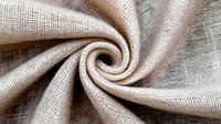 Natural beige linen fabric with loose weave texture twisted in elegant spiral fold, showcasing organic textile material for home decor and craft projects.