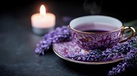 Cup of herbal lavender tea in vintage porcelain teacup with fresh purple lavender flowers and glowing candle on dark background, moody atmosphere.