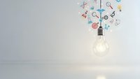 Glowing light bulb with colorful business icons floating above on clean white background representing creative ideas and innovation concepts.