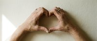 Elderly hands forming a heart shape against a light wall, symbolizing love, care, and compassion in senior life and relationships.