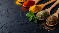 Colorful spices in wooden spoons on dark slate background with fresh mint leaves. Cooking ingredients for culinary recipes and healthy meal preparation.