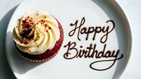 Red velvet cupcake with cream frosting on white plate, Happy Birthday written in chocolate sauce, top view, celebration dessert concept.