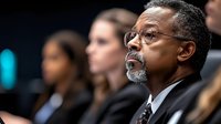 Mature African American businessman with glasses and gray beard listening attentively during corporate meeting or conference presentation.