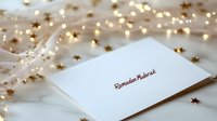 White greeting card with Ramadan Mubarak text surrounded by golden star decorations and warm fairy lights on soft fabric, creating festive holiday atmosphere.