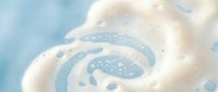 Creamy white foam swirls with bubbles on soft blue background for skincare cosmetics and spa wellness product advertising.