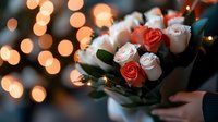 Romantic bouquet of coral and white roses held against blurred bokeh lights background, creating dreamy atmosphere for Valentine's day or wedding celebration.