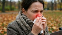Young Caucasian woman with cold or flu symptoms blowing nose with tissue in autumn park. Seasonal illness, healthcare and wellness concept for medical use.