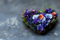 Heart-shaped floral arrangement with vibrant pansies in purple, blue and orange tones on dark stone background, romantic garden composition for Valentine's day or wedding decor.