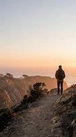 Hiker with backpack standing on rocky cliff overlooking ocean at sunset, enjoying coastal landscape and adventure travel experience.